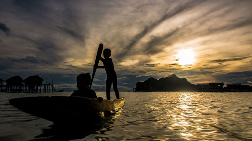 Silhouette children rowing boat in river during sunset