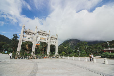 People at historical building in city against cloudy sky