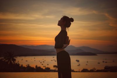 Side view of woman practicing yoga at beach during sunset