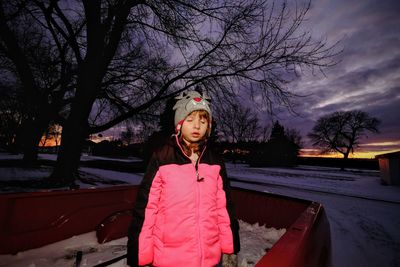 Portrait of young woman standing against bare trees during winter