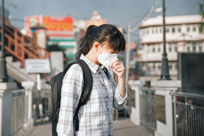 Woman wearing pollution mask while standing on footpath