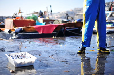 Low section of man standing by fish in container at harbor