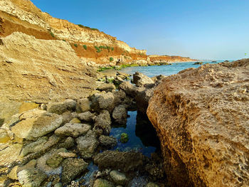 Rock formations by sea against clear blue sky