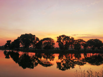 Silhouette trees by lake against sky during sunset