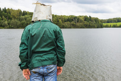 Rear view of man standing by river against sky