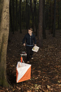 Full length of boy holding map while standing in forest