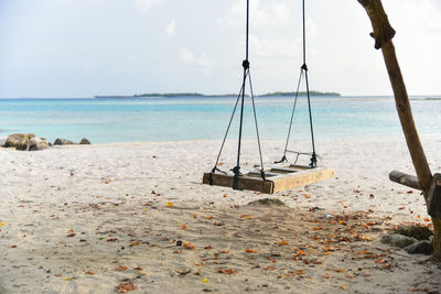 Swing hanging on beach against sky