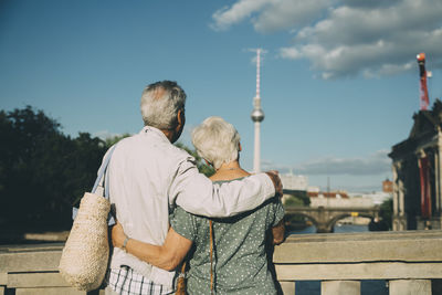 Rear view of senior couple with arm around looking at television tower from bridge in city