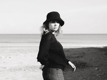 Young woman standing at beach against sky