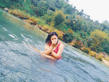 Cheerful woman covering mouth sitting in lake