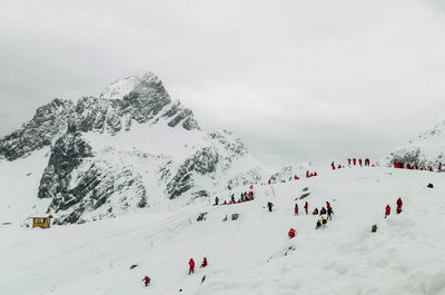 Scenic view of people skiing against cloudy sky