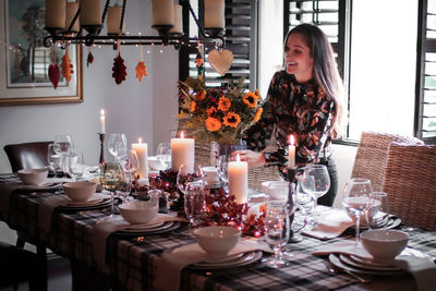 Smiling mid adult woman holding arranging flower vase on dinning table at home