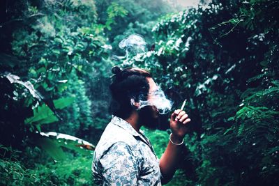 Man smoking cigarette against trees