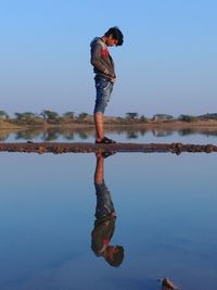 Young woman standing by lake against clear blue sky