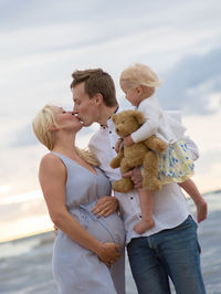 Man with daughter kissing pregnant woman at beach