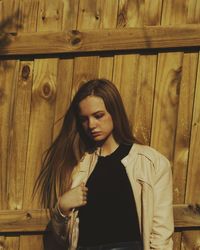 Young woman looking down standing against wooden fence