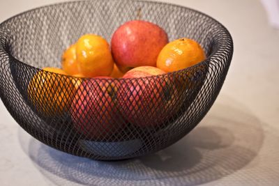 Apples and mandarins in a wire bowl inside on a kitchen bench