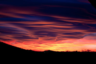 Silhouette landscape against dramatic sky during sunset