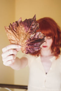 Woman with dry leaf standing against wall