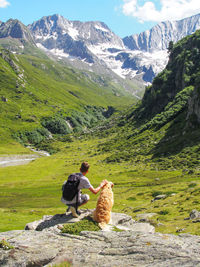 Rear view of teenage boy with dog against mountains on rock