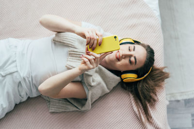 Directly above shot of woman listening music while lying down on bed at home