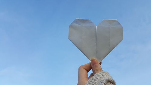 Low angle view of hand holding heart shape against blue sky