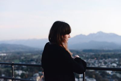 Young woman standing by railing against sky