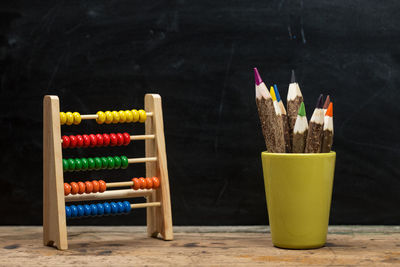 Close-up of colored pencils in desk organizer by abacus on table against black background