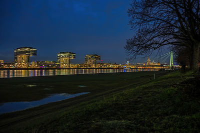 Illuminated buildings by river against sky at night