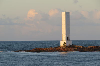 Lighthouse by sea against sky during sunset