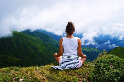 Rear view of woman sitting on cliff against cloudy sky