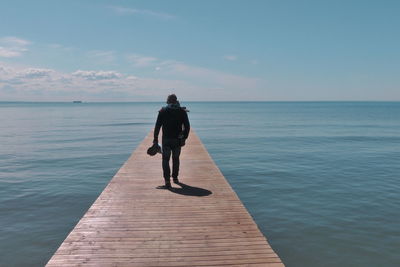 Rear view of man walking on pier over sea against sky