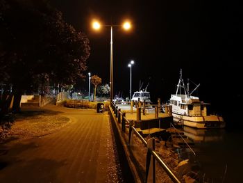 Illuminated street by road against sky at night