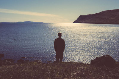 Rear view of silhouette man standing by sea against sky