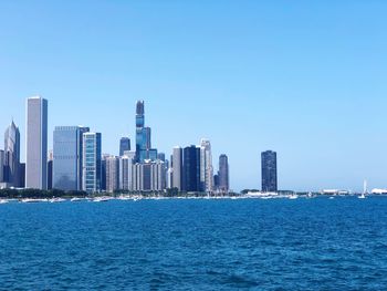 Sea by modern buildings against clear blue sky