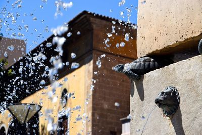 Low angle view of water drops on built structure against sky