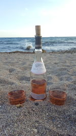 Bottles on beach by sea against sky