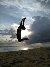 Woman jumping at beach against sky during sunset