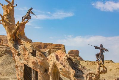 Low angle view of statues on bare tree at desert against sky