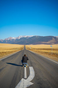 Rear view of man walking on road against clear blue sky