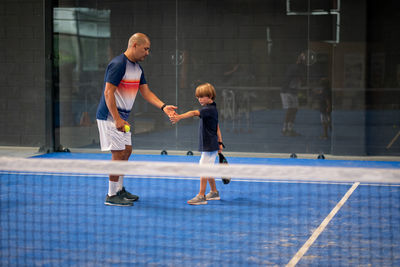 Monitor teaching padel class to child, his student - trainer teaches little boy how to play padel 