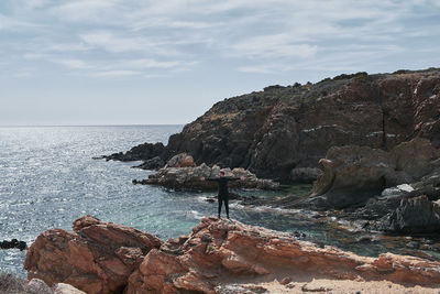 Man standing on cliff by sea against sky