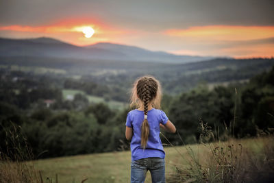 Rear view of boy standing on field during sunset