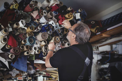 Low angle view of senior male owner looking at rolled fabrics in workshop