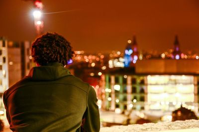 Rear view of a man on balcony looking at city at night