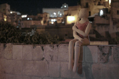 Side view of shirtless boy sitting on retaining wall at night