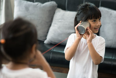 Cute sisters playing with tin can phone at home