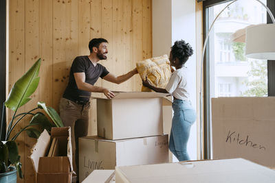 Happy couple removing cushion from cardboard box at new home