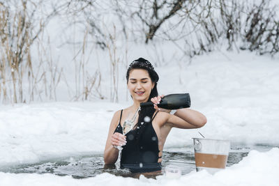 Portrait of young woman drinking water while standing on snow