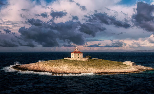 View of lighthouse on beach against cloudy sky